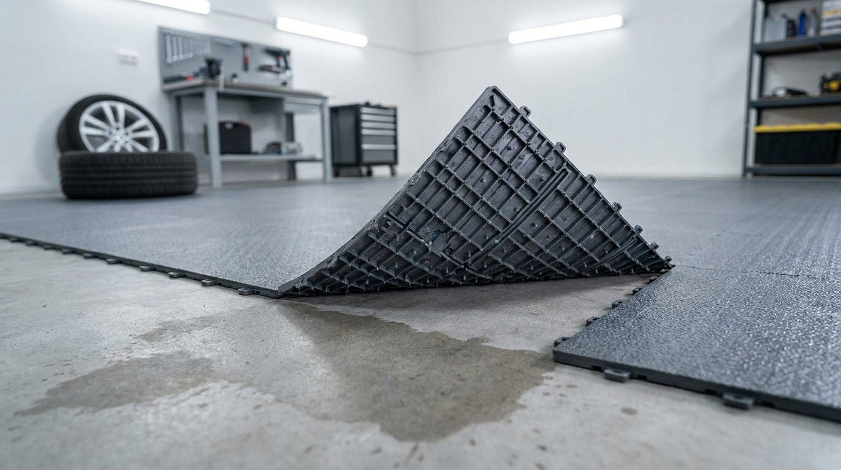 Garage ou atelier automobile avec un revêtement de sol modulaire gris soulevé et déformé, illustrant les risques d'un sol de garage humide.