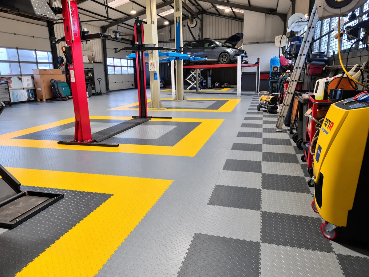 Détail du sol du garage Auto Diffusion 44 : dalles tôle larmée gris clair, bande jaune de sécurité et damier gris foncé le long des établis