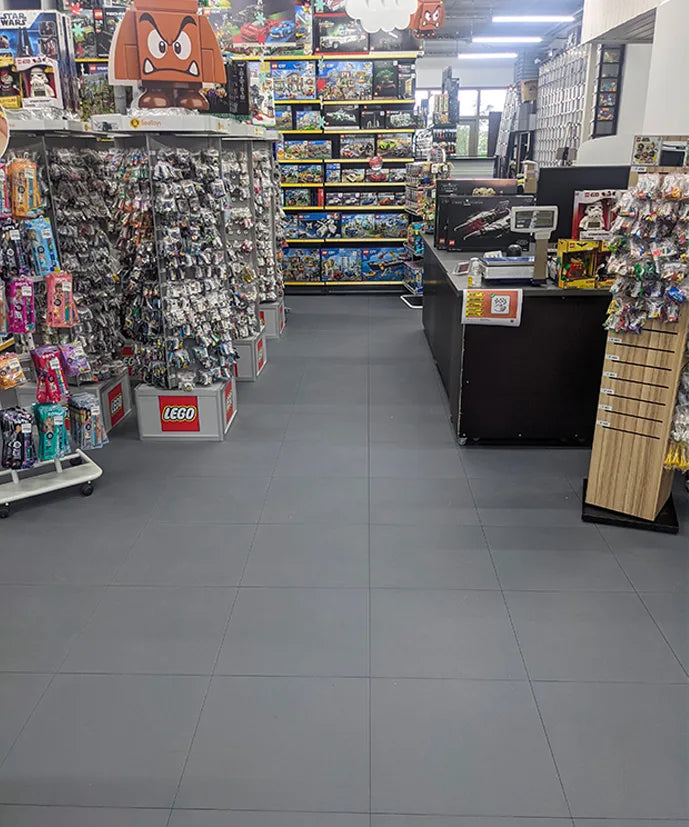 Magasin de jouets BEETOYS à Perly-Certoux : allée centrale et caisse sur dalles PVC ULTIMA JOINTS INVISIBLES PURE gris foncé