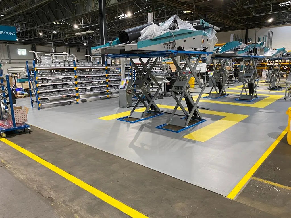 Usine EXOTEC après pose : zone de montage en dalles PVC ULTIMA INDUSTRY PURE gris clair avec repères jaunes autour des élévateurs