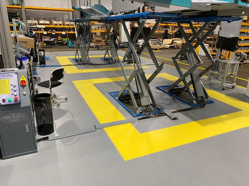 Détail du calepinage gris clair et jaune en dalles ULTIMA INDUSTRY autour d'une table élévatrice, EXOTEC