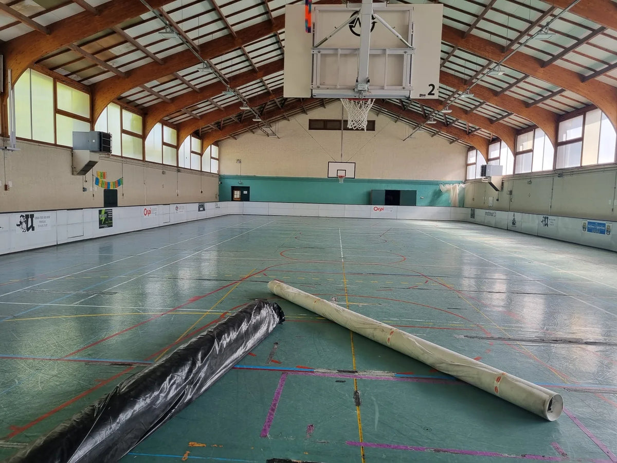 Gymnase de Royan avant travaux : ancien sol sportif usé aux marquages superposés, rouleaux de géotextile